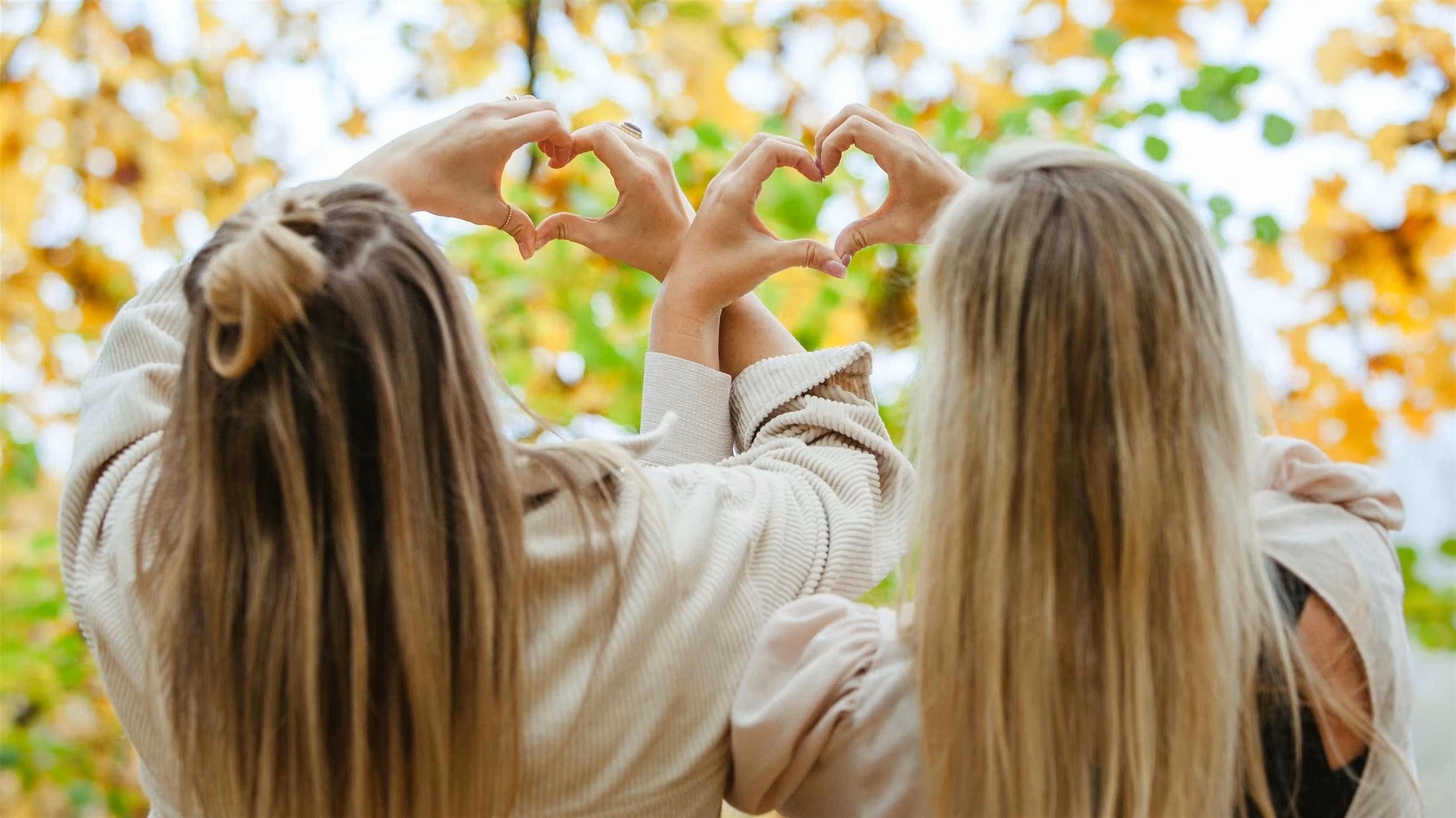 Zwei Frauen formen mit ihren Händen ein Herz im herbstlichen Licht